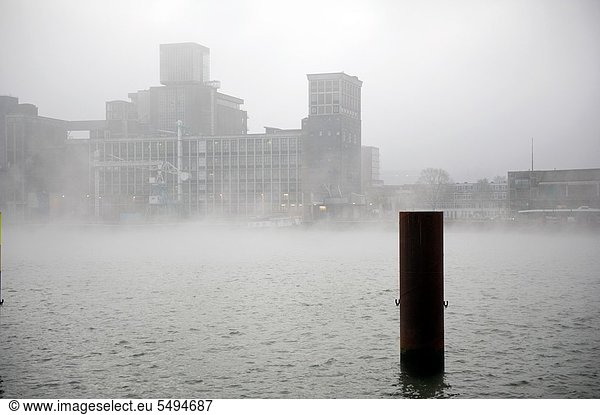 The Rotterdam Rijnhaven is foggy on this morning in november. The factory opposite of the water is barely visible. Image taken from the docks.