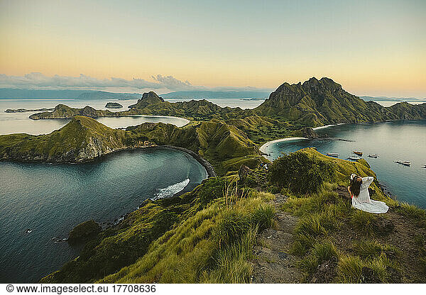 The rugged coastline of Padar Island  Indonesia with a young woman on the ridge above looking out to the sunset and tranquil ocean  Komodo National Park; Padar Island  East Nusa Tenggara  Indonesia