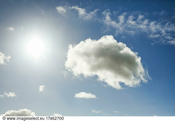 The sun shines next to an cumulus cloud (Cumulus) cloud and a few feather clouds in the blue sky