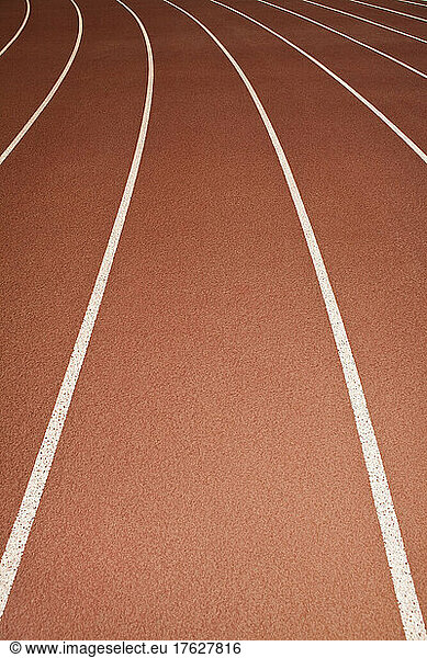 The surface of a sports athletics running track  red surface with white painted lane markings.