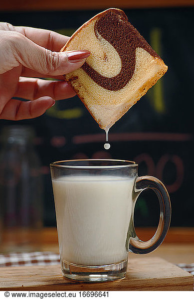 The woman's hand dip the marble cake into the milk in a glass of milk