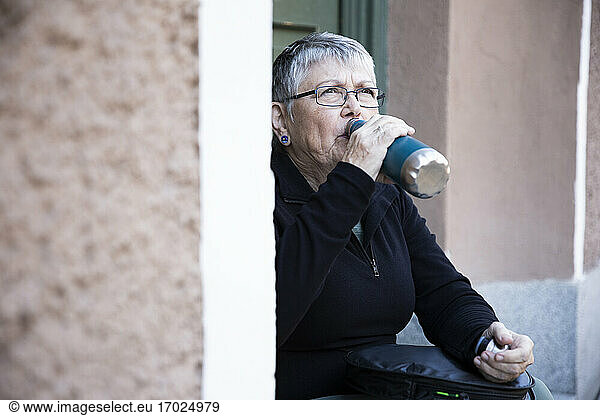 Thirsty woman drinking water from bottle at doorway