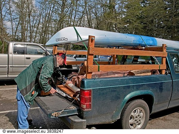 This middle aged Caucasian man is preparing the back of his truck with camping gear with a kayak loaded on top in readiness for a camping trip