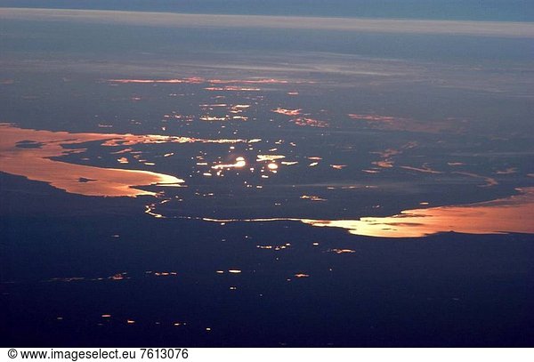 This strongly oblique from the side view shows the Gulf of Finland and Lake Ladoga in the late afternoon. At this time of day  sunglint—the reflection of sunlight into the camera lens—distinguishes the bodies of water from their surroundings. The image was taken from the International Space Station when the craft orbited north of the Caspian Sea  approximately 2 500 kilometers 1600 miles to the southeast on the Russia_Kazakhstan border. Lakes in Finland in the middle of the view are 3 000 kilometers 1900 miles from the camera. The Neva River appears in sunglint  connecting Lake Ladoga to the gulf. Czar Peter the Great constructed St. Petersburg  starting in 1703  on the Neva River Delta. He established this city as his capital and window into Europe via the Baltic Sea. Although not visible  St. Petersburg—the home town of Sergei Krikalev  Space Station commander when this picture was taken—lies on the Neva River delta. In this view  taken with a powerful 400_millimeter lens  sunglint even reveals the causeways to Kotlin Island in the gulf—including some of the details of their construction. Oblique views reveal marked layers of gray haze generated by air pollution top image  top of view  a common sight over Western Europe. Pollution also renders the bright glint areas a coppery color. Below the photographs are a satellite view of St. Petersburg left and a map showing the location of the International Space Station at the time the photograph was taken right.