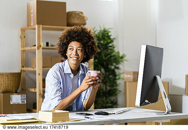 Thoughtful Afro businesswoman holding mug at desk in studio