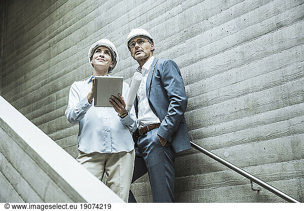 Thoughtful architects standing with tablet PC on staircase