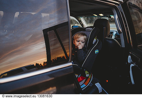 Thoughtful baby boy sitting on cat seat during sunset