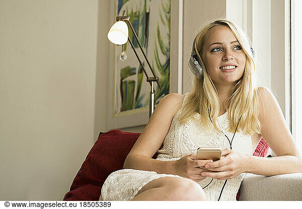 Thoughtful beautiful young woman listening to music and sitting on sofa in the living room  Munich Bavaria  Germany