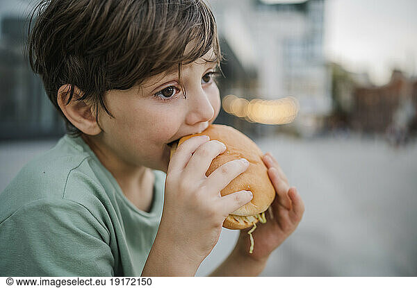 Thoughtful boy eating burger at street