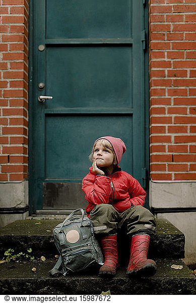 Thoughtful boy in warm clothing sitting on steps