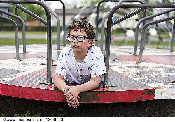 Thoughtful boy lying on merry-go-round at playground