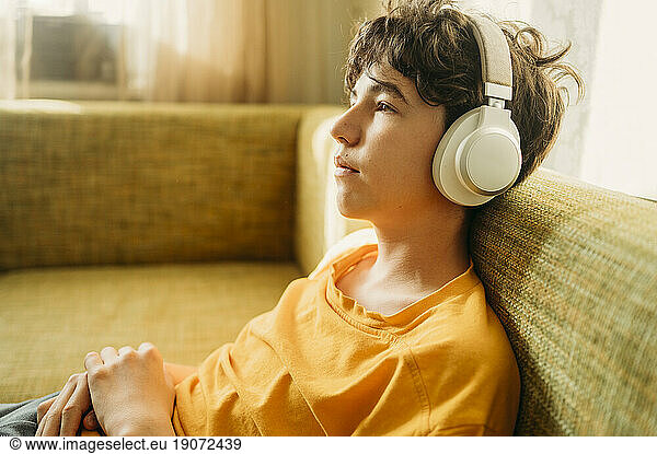 Thoughtful boy with headphones relaxing on sofa