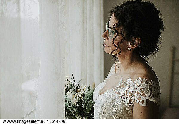 Thoughtful bride with bouquet looking out of window