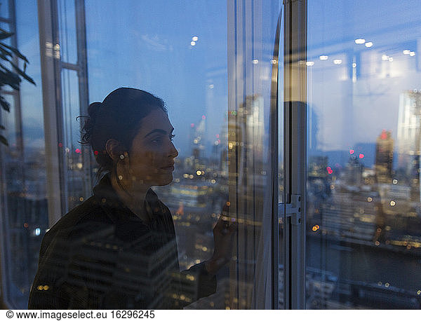 Thoughtful business woman working late at highrise office window