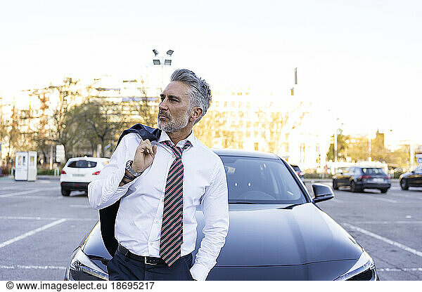 Thoughtful businessman carrying blazer standing near car