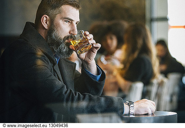 Thoughtful businessman drinking alcohol in hotel seen though window