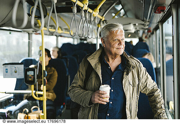 Thoughtful businessman holding disposable cup while commuting through bus