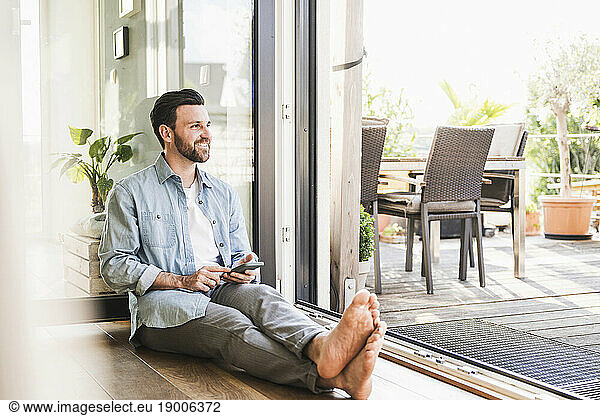 Thoughtful businessman sitting with smart phone on floor