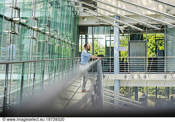 Thoughtful businessman standing at railing in modern office building