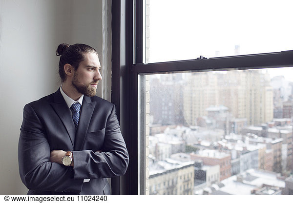 Thoughtful businessman standing with arms crossed while looking through window