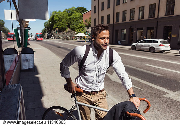 Thoughtful businessman standing with bicycle on sidewalk in city