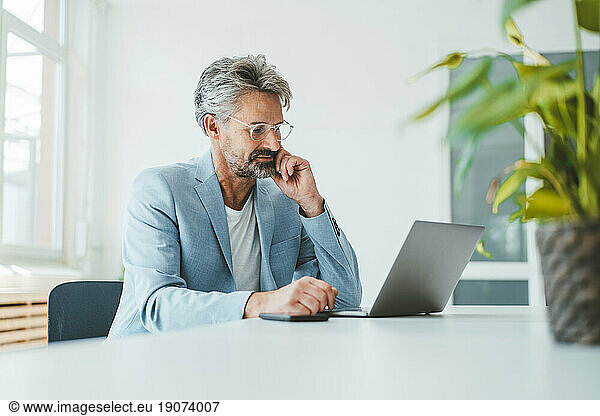 Thoughtful businessman using laptop at desk in office
