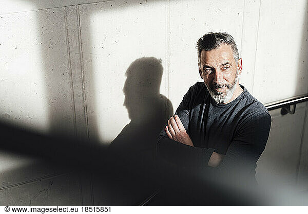 Thoughtful businessman with arms crossed standing in front of wall