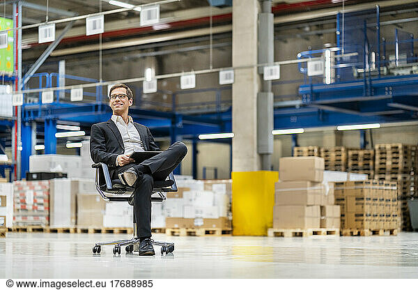 Thoughtful businessman with leg crossed at knee in warehouse
