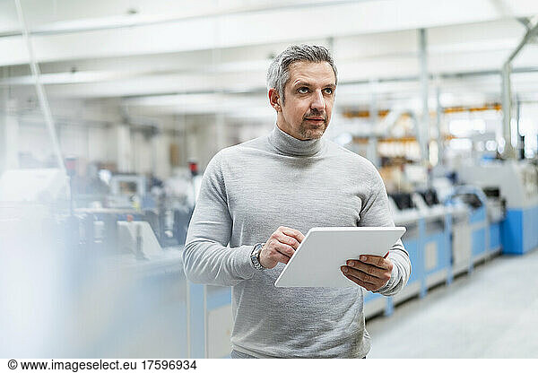 Thoughtful businessman with tablet PC in factory