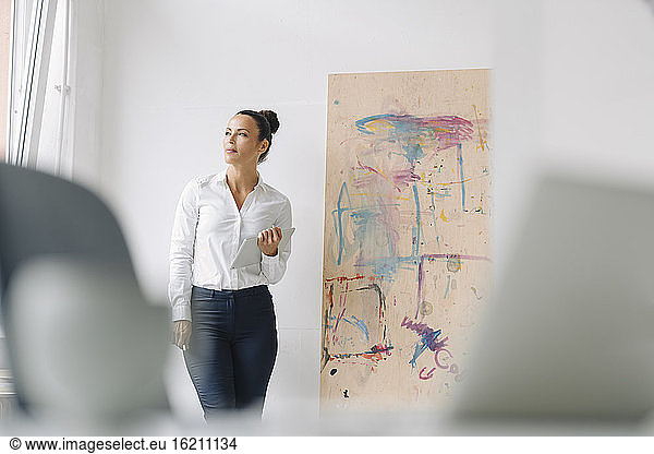 Thoughtful businesswoman holding digital tablet while standing against wall in home office