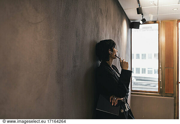 Thoughtful businesswoman looking away while leaning on wall at office