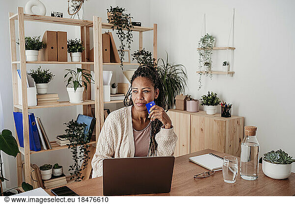 Thoughtful businesswoman sitting with credit card at desk