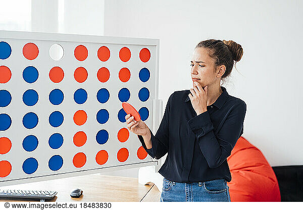 Thoughtful businesswoman standing by connect four game rack in office