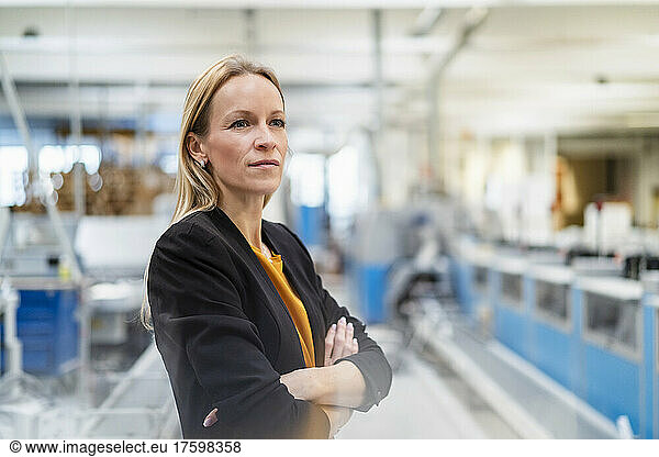 Thoughtful businesswoman standing with arms crossed in factory
