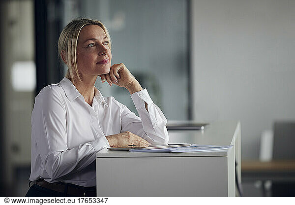 Thoughtful businesswoman standing with hand on chin by cabinet in office
