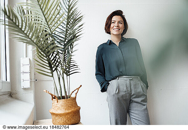 Thoughtful businesswoman standing with hands in pockets at office