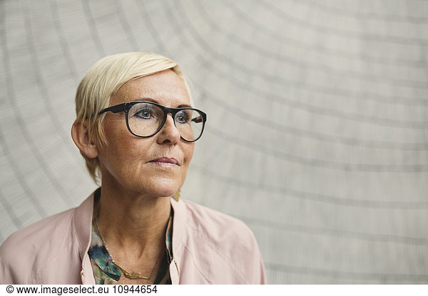 Thoughtful businesswoman wearing eyeglasses against wall