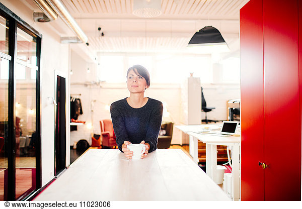 Thoughtful businesswoman with coffee mug at desk in office
