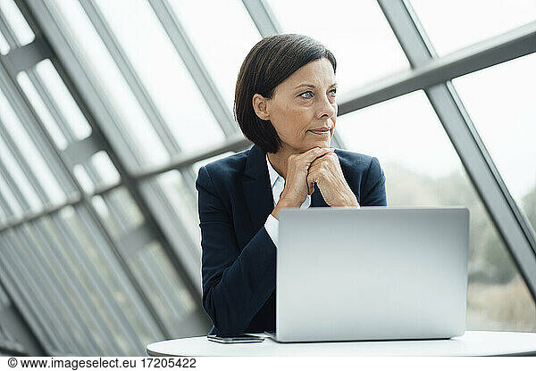 Thoughtful businesswoman with hand on chin by laptop at desk in office