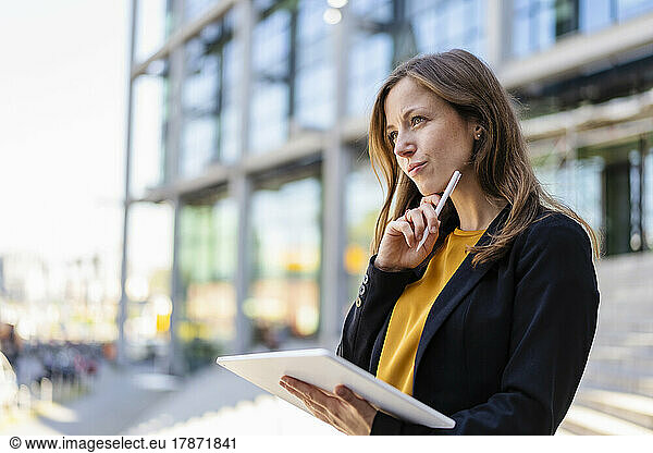 Thoughtful businesswoman with hand on chin holding tablet PC and digitized pen