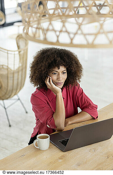 Thoughtful businesswoman with hand on chin sitting by laptop in office