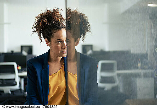 Thoughtful businesswoman with reflection on glass wall in office