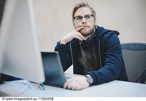 Thoughtful computer programmer sitting at desk in office