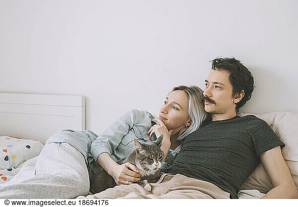 Thoughtful couple with cat lying on bed at home