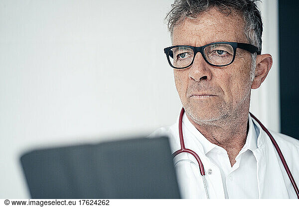 Thoughtful doctor with stethoscope by wall