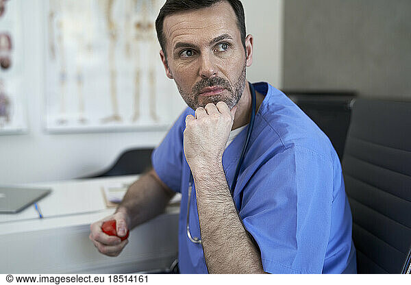 Thoughtful doctor with stress ball sitting in clinic