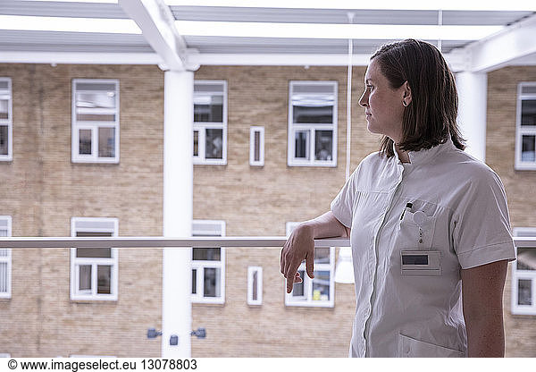 Thoughtful female doctor looking away while standing by railing in hospital