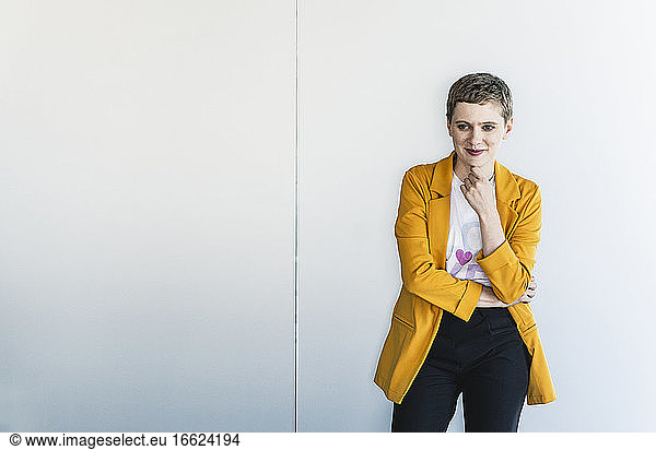 Thoughtful female entrepreneur wearing yellow blazer standing against wall in office