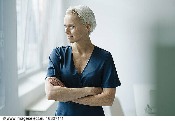 Thoughtful female entrepreneur with arms crossed looking away while standing in office