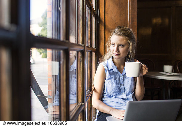 Thoughtful freelancer looking through window while using laptop at cafe